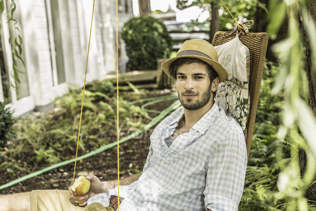 Jeune homme assis sur hamac dans le jardin — Photo de stock