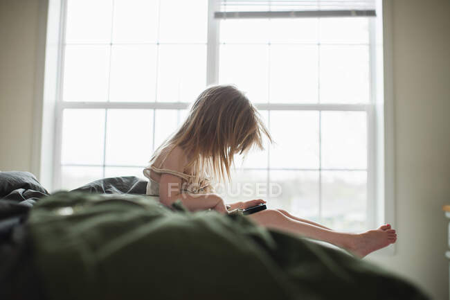 Девушка сидит на кровати с помощью смартфона — стоковое фото