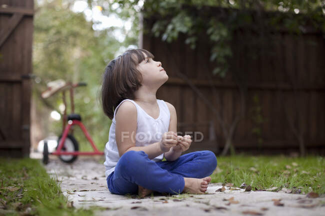 Четырехлетняя девочка сидит на садовой дорожке и смотрит вверх. — стоковое фото