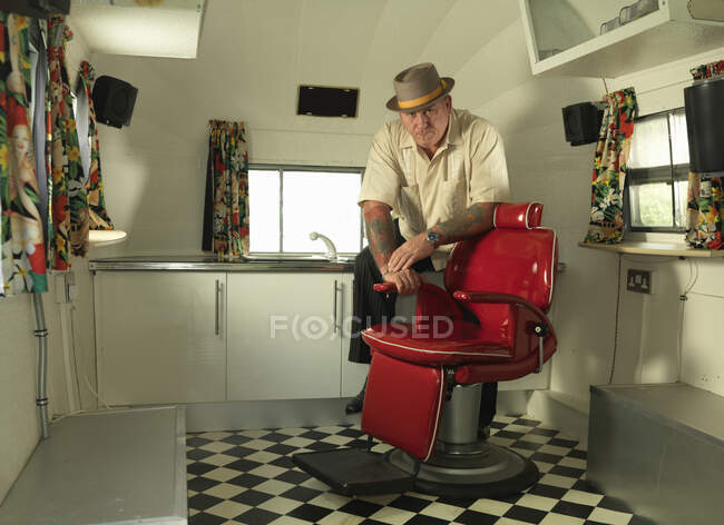 Tatoueur dans un salon de tatouage mobile portant un chapeau à tarte au porc regardant la caméra — Photo de stock