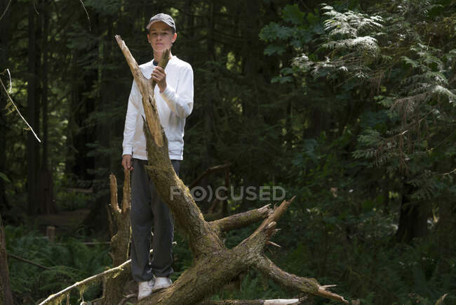 Adolescent assis sur un tronc d'arbre tombé regardant une caméra, parc national Pacific Rim, île de Vancouver, Canada — Photo de stock