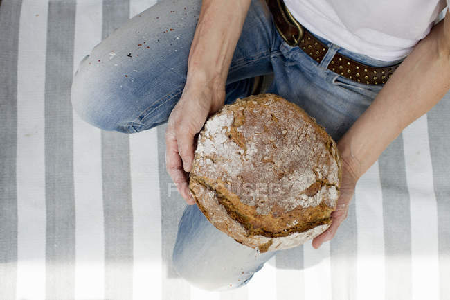 Cropped image of woman holding fresh baked bread on striped rug — Stock Photo