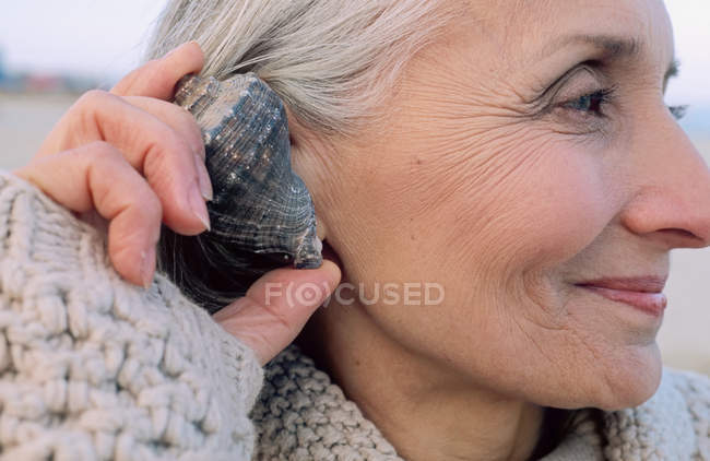 Donna anziana che tiene un guscio all'orecchio — Foto stock
