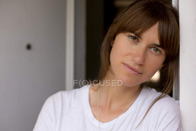 Portrait of mid adult woman leaning against doorframe, looking at camera — Stock Photo