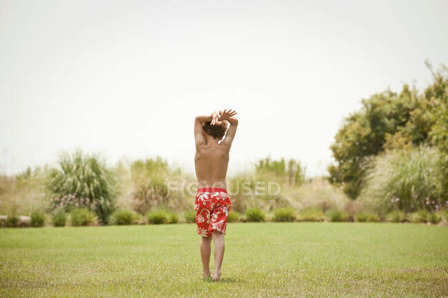 Мальчик в купальнике ходит по травянистому полю — стоковое фото