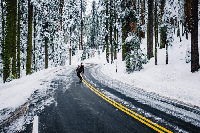 Skateboarder travelling on road in winter landscape, Sequoia National Park, California, USA — Stock Photo