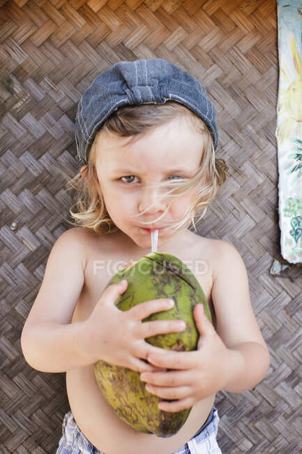 Portrait of male toddler in baseball cap drinking coconut milk — Stock Photo
