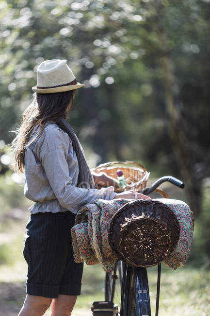 Mulher madura olhando para a floresta com bicicletas e cestas de forrageamento — Fotografia de Stock