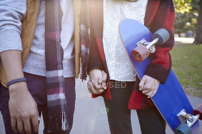 Mid section of young woman skateboarder holding hands with boyfriend in park — Stock Photo
