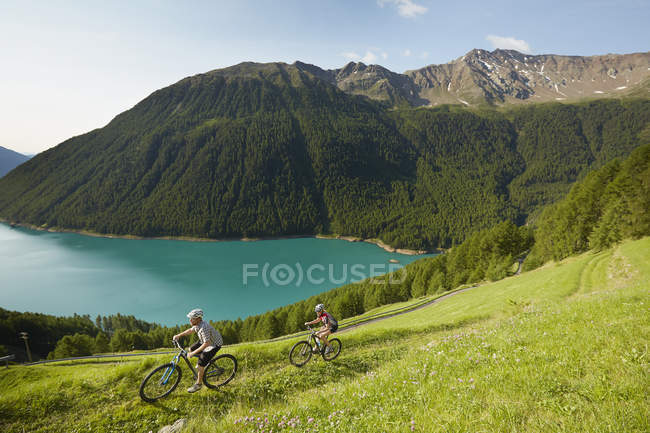 Pareja joven ciclismo de montaña en el embalse de Vernagt, Val Senales, Tirol del Sur, Italia - foto de stock