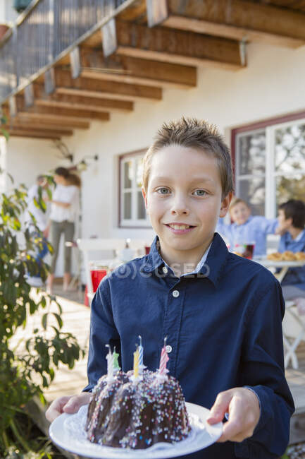 Retrato de niño llevando pastel de cumpleaños en el patio - foto de stock