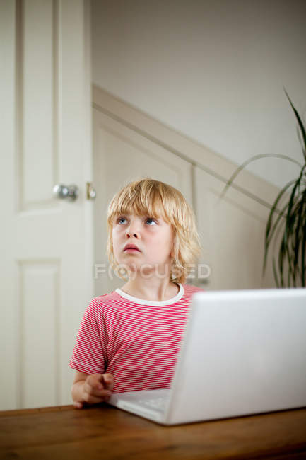 Niño mirando desde el ordenador portátil en el escritorio - foto de stock