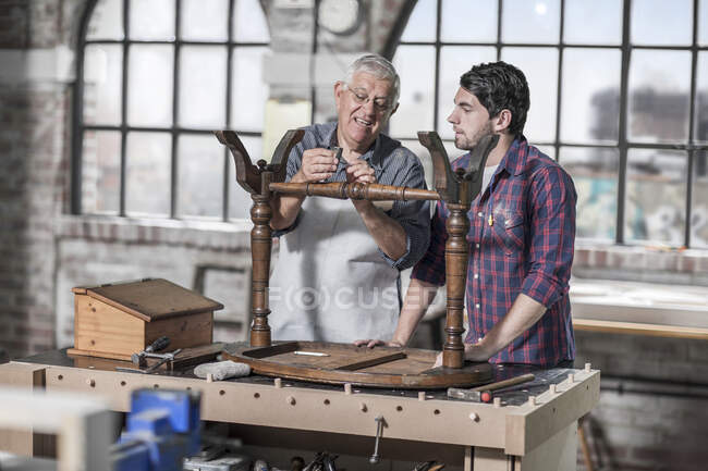 Cape Town, South Africa, elderly craftsman explaining to co worker while working on wooden table — Stock Photo