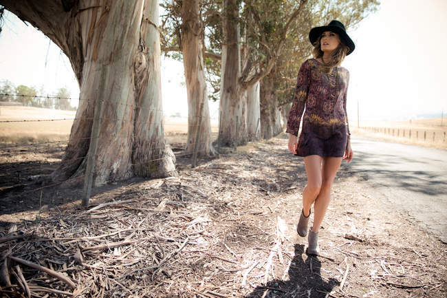 Young woman in boho style and felt hat strolling on roadside — Stock Photo
