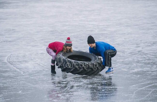 Paar kippt Reifen auf zugefrorenem See — Stockfoto