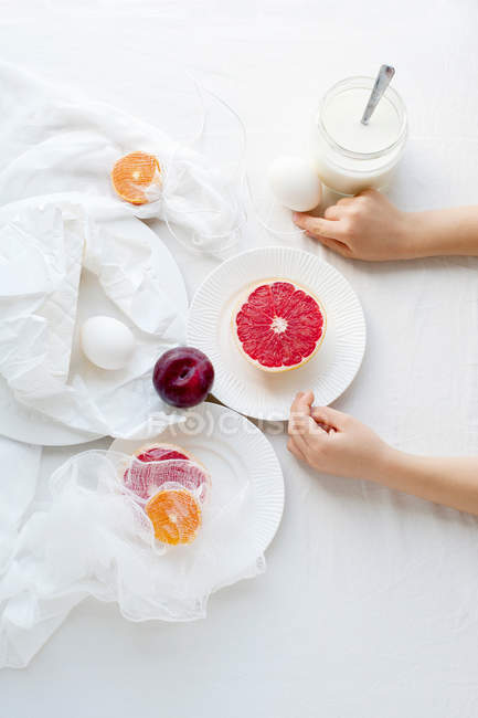 Imagen recortada de niño sentado a la mesa con frutas y leche - foto de stock
