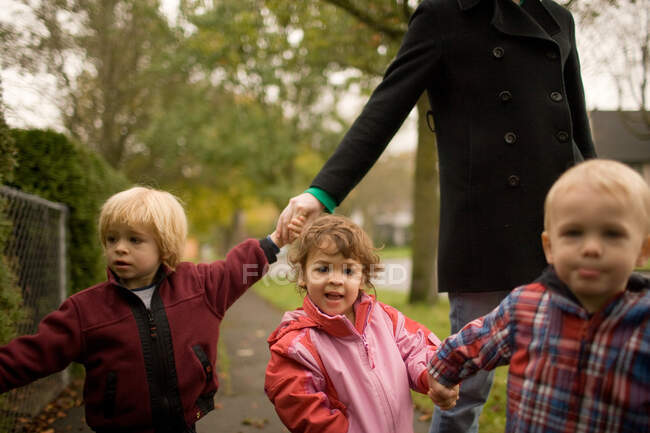 Femme avec trois enfants marchant le long du trottoir — Photo de stock