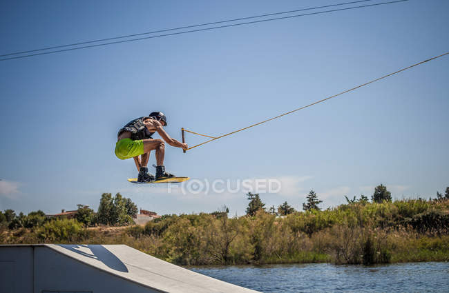 Media adulto macho wakeboarder salto rampa en el mar, Cagliari, Cerdeña, Italia - foto de stock