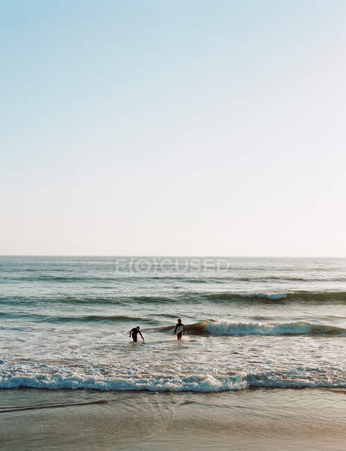 Surfers walking in waves on beach — Stock Photo