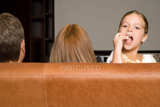 Chica comiendo palomitas de maíz con la familia - foto de stock