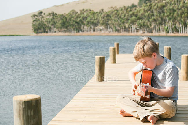 Мальчик играет на гитаре на пирсе — стоковое фото