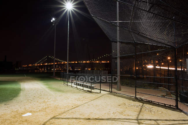 Empty Baseball playground in the evening with illuminated bridge on background — Stock Photo