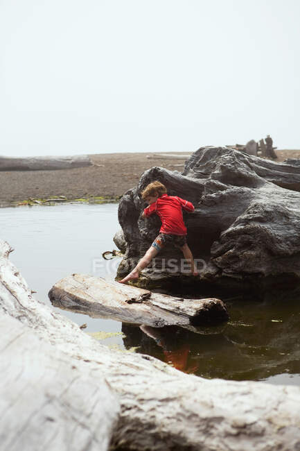 Niño escalando en trozos de madera a la deriva - foto de stock