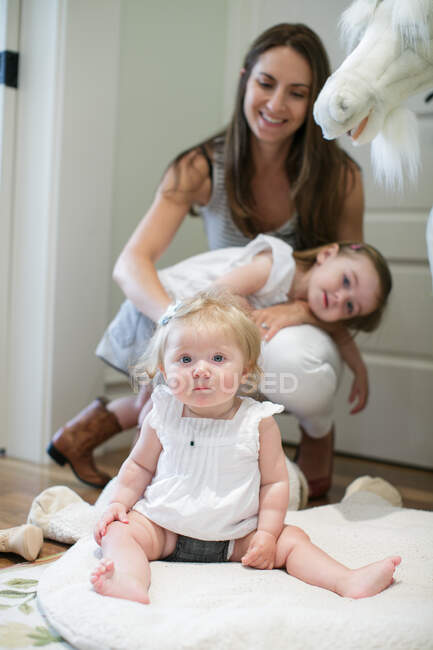 Retrato de niña sentada en el suelo con madre y hermana detrás - foto de stock