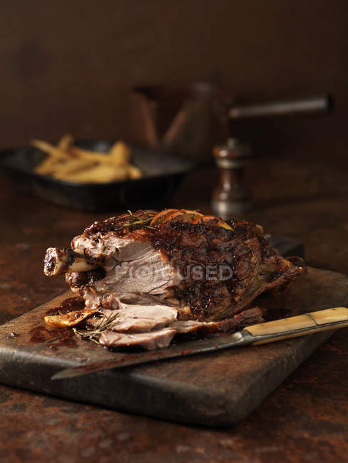 Carved roasted lamb on kitchen table with french fries — Stock Photo
