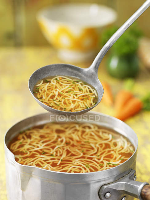 Close up of saucepan and ladle with noodle soup — Stock Photo