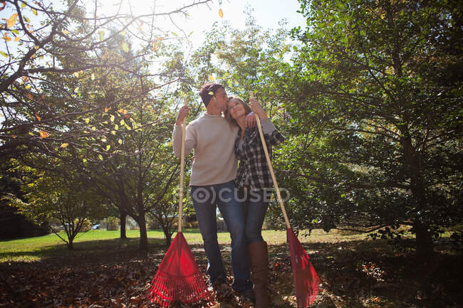 Affectionate couple with leaf rakes — Stock Photo