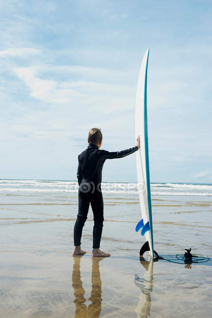 Мальчик смотрит в море с доской для серфинга — стоковое фото