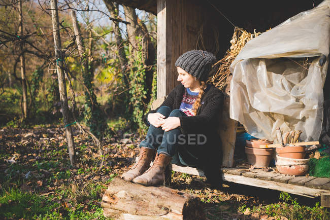 Jeune femme assise dans un hangar de stockage portant un chapeau en tricot détournant les yeux — Photo de stock