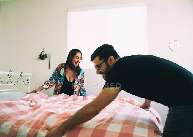 Happy couple making bed together — Stock Photo