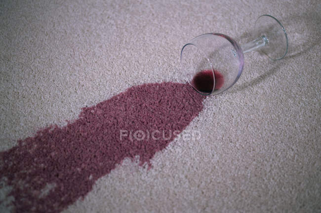 Verre avec tache de vin rouge sur un tapis — Photo de stock