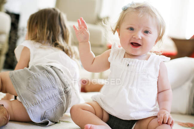 Portrait of baby girl sitting on floor with sister behind — Stock Photo