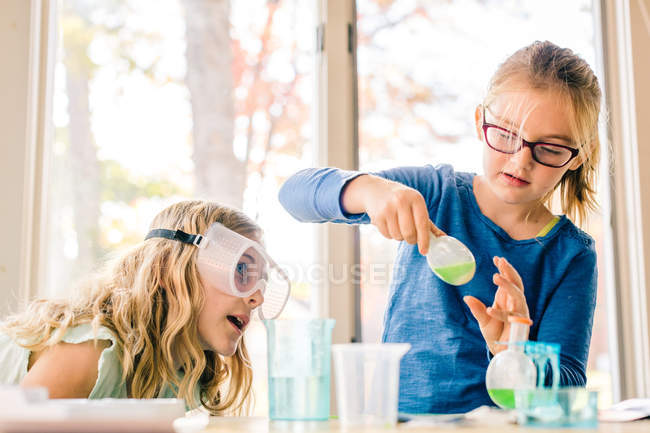 Дві дівчинки проводять науковий експеримент, трясучи рідину у колбі. — стокове фото
