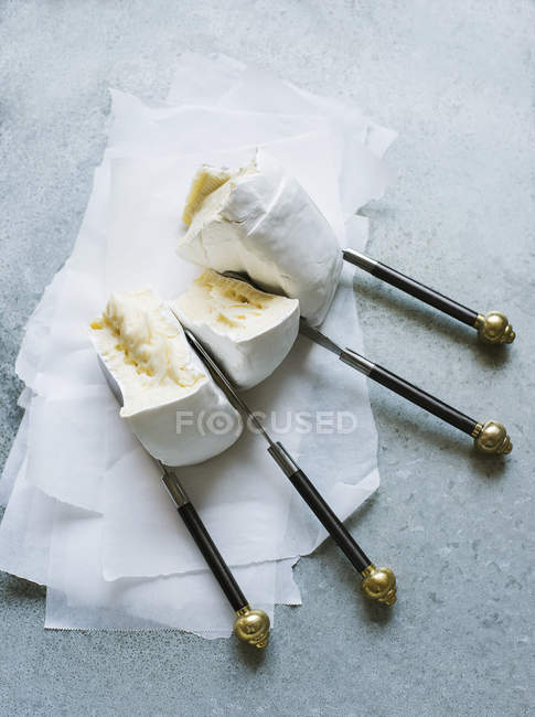 Hochwinkelaufnahme von Brie-Stücken, die mit Messern auf fettdichtem Papier getrennt werden — Stockfoto