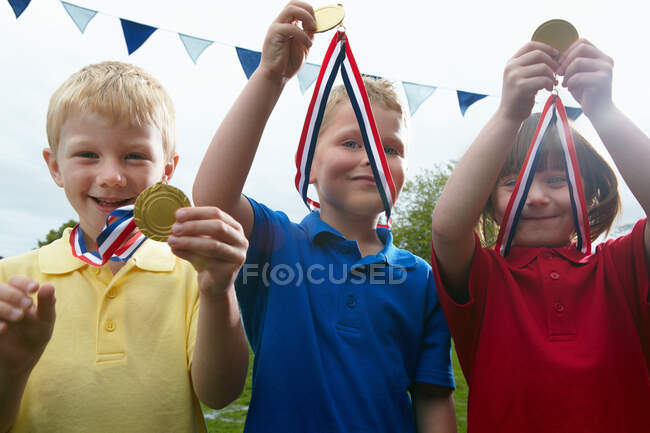 Três crianças segurando medalhas esportivas no campo de jogo da escola — Fotografia de Stock