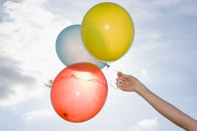 Mano tenendo palloncini colorati con cielo nuvoloso blu sullo sfondo — Foto stock