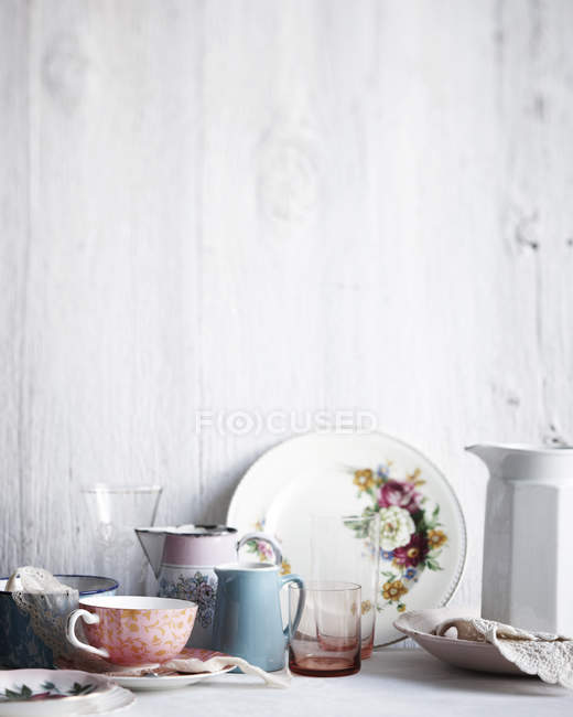 Verschiedene Trinkgläser, Teller und Krüge auf weißgetünchtem Tisch — Stockfoto