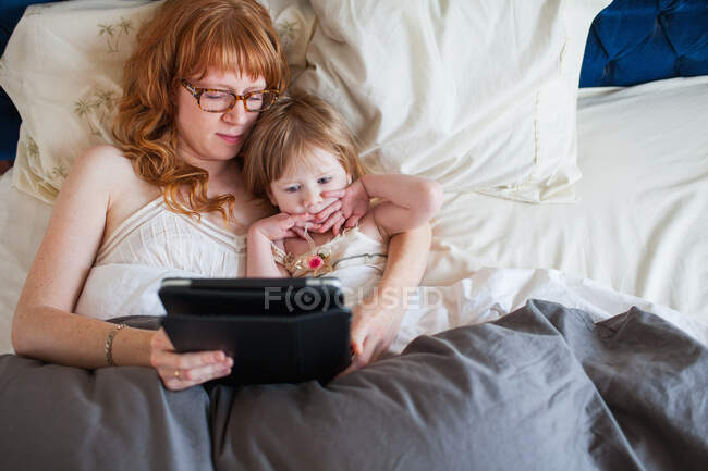 Мати і дочка лежать в ліжку, дивлячись на цифровий планшет — стокове фото