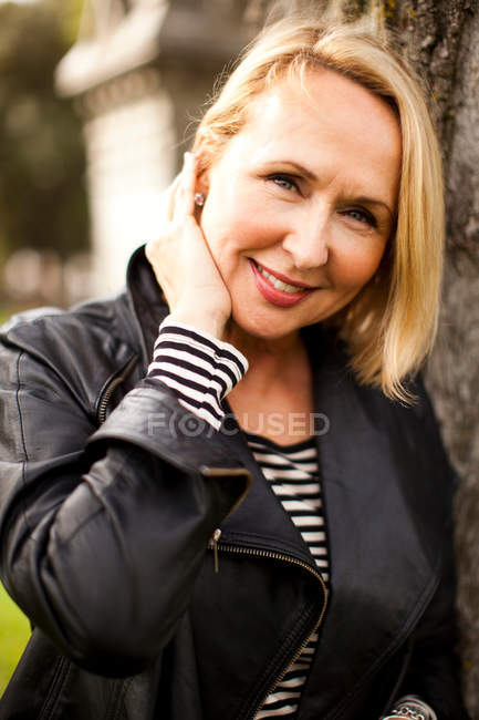 Mulher madura vestindo jaqueta de couro e sorrindo no parque, retrato — Fotografia de Stock