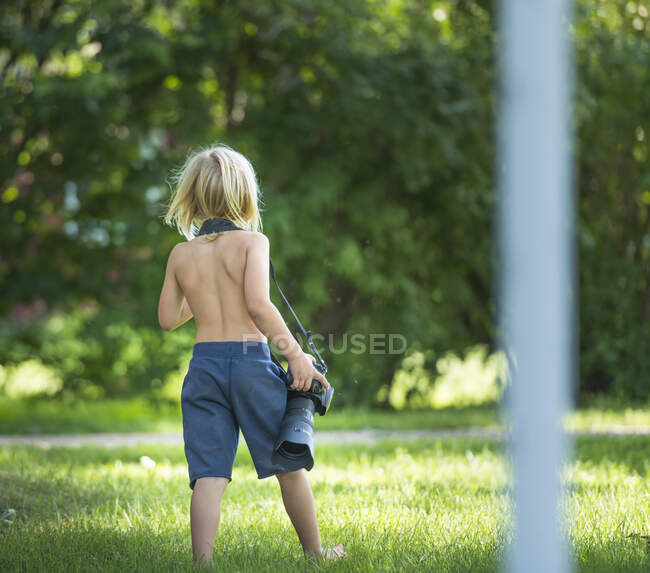 Rear view of boy carrying camera — Stock Photo
