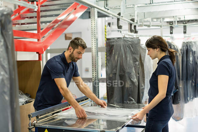 Trabalhadores do armazém que embrulham o estoque de vestuário em plástico no armazém de distribuição — Fotografia de Stock