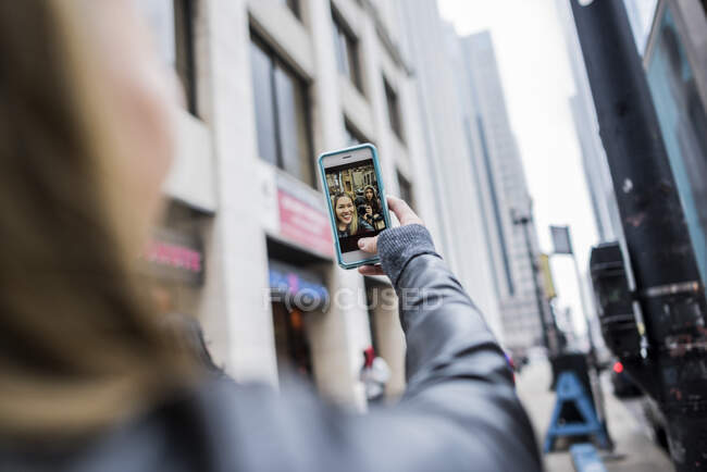 Молодая женщина, на улице, держит смартфон, на видеовызове, вид сзади — стоковое фото