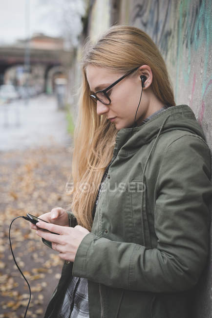 Jeune femme utilisant un smartphone par mur de graffiti — Photo de stock
