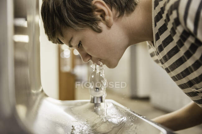 Мальчик-подросток, пьющий из питьевого фонтана в школе — стоковое фото
