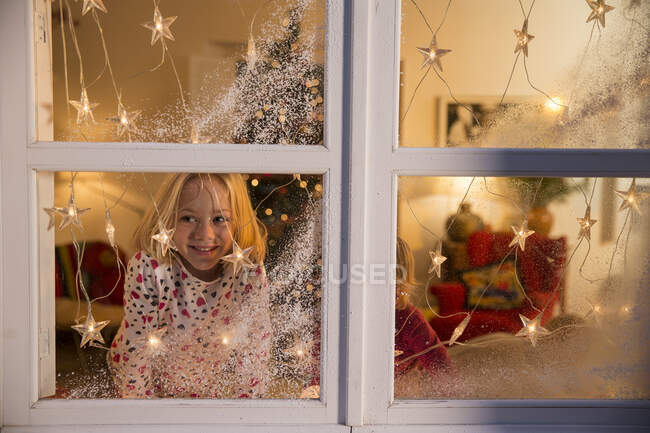 Ragazza che guarda fuori dalla finestra con decorazioni natalizie — Foto stock