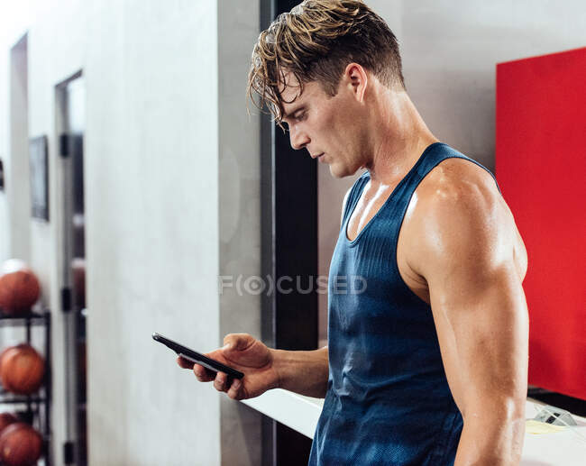 Sudor jugador de baloncesto masculino mirando el teléfono inteligente en el vestuario - foto de stock